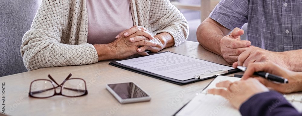 Elderly Couple sitting at a desk with a financial advisor and papers on the desk between them.
